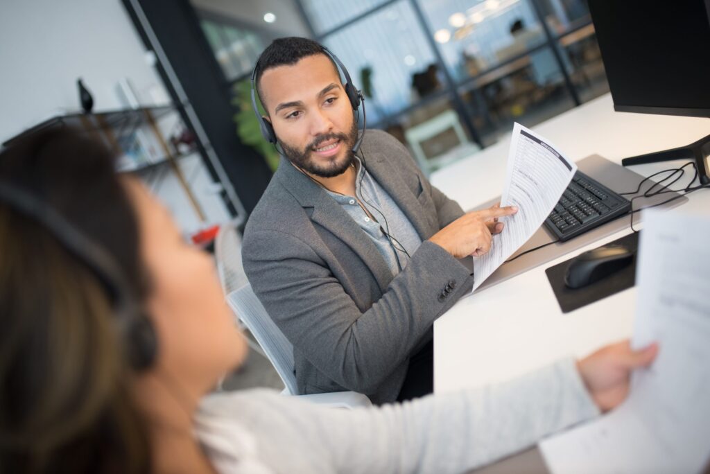 Colleagues discussing documents with headsets in a modern office setting.